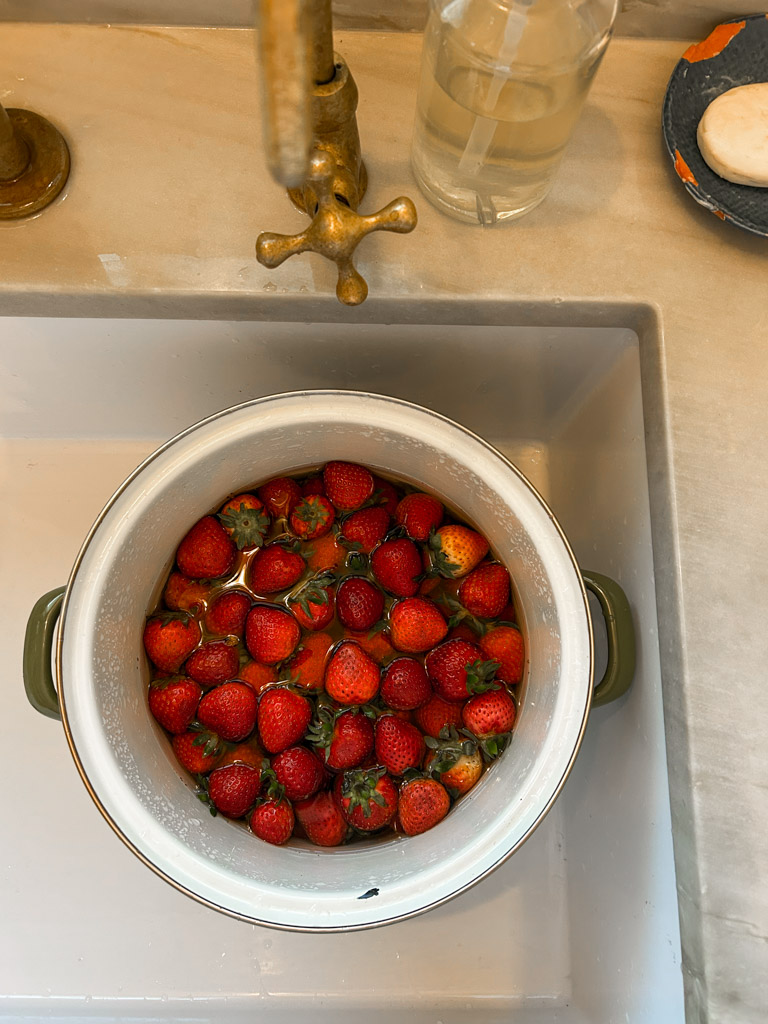 Strawberries being washed in a white colander in a sink