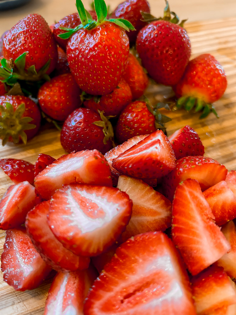red ripe strawberries being cut on a wooden cutting board