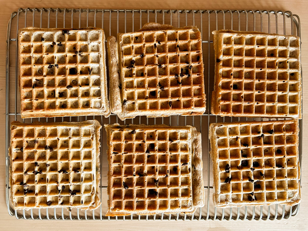 six belgian spelt waffles sit on a wire rack to cool on the counter