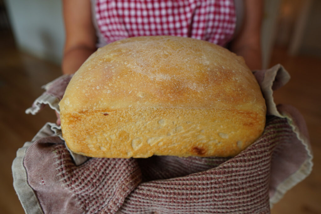 Girl in a red and white apron holding a loaf of sourdough sandwich bread