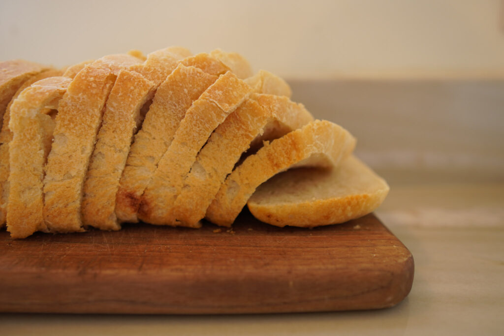 Sliced sourdough sandwich bread sitting on a wooden bread board on a white countertop