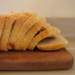 Sliced sourdough sandwich bread sitting on a wooden bread board on a white countertop