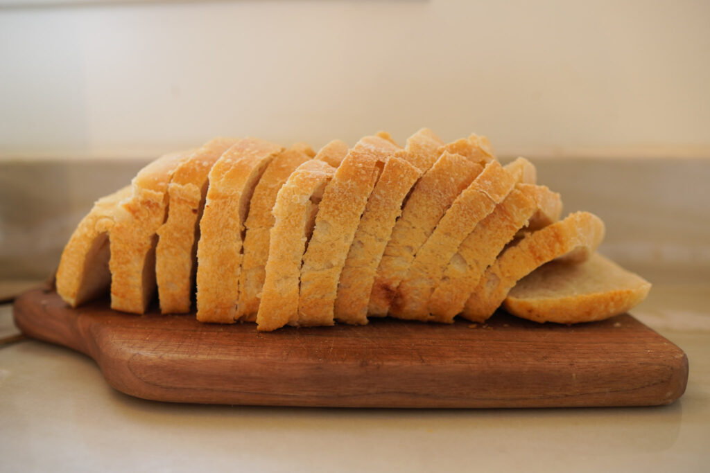Sliced sourdough sandwich bread sitting on a wooden bread board on a white countertop