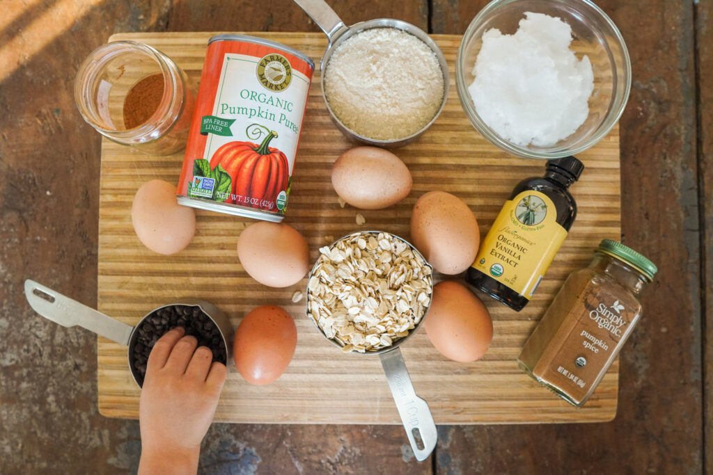 ingredients for pumpkin muffins sitting on a wooden cutting board including canned pumpkin, oats, eggs, and flour