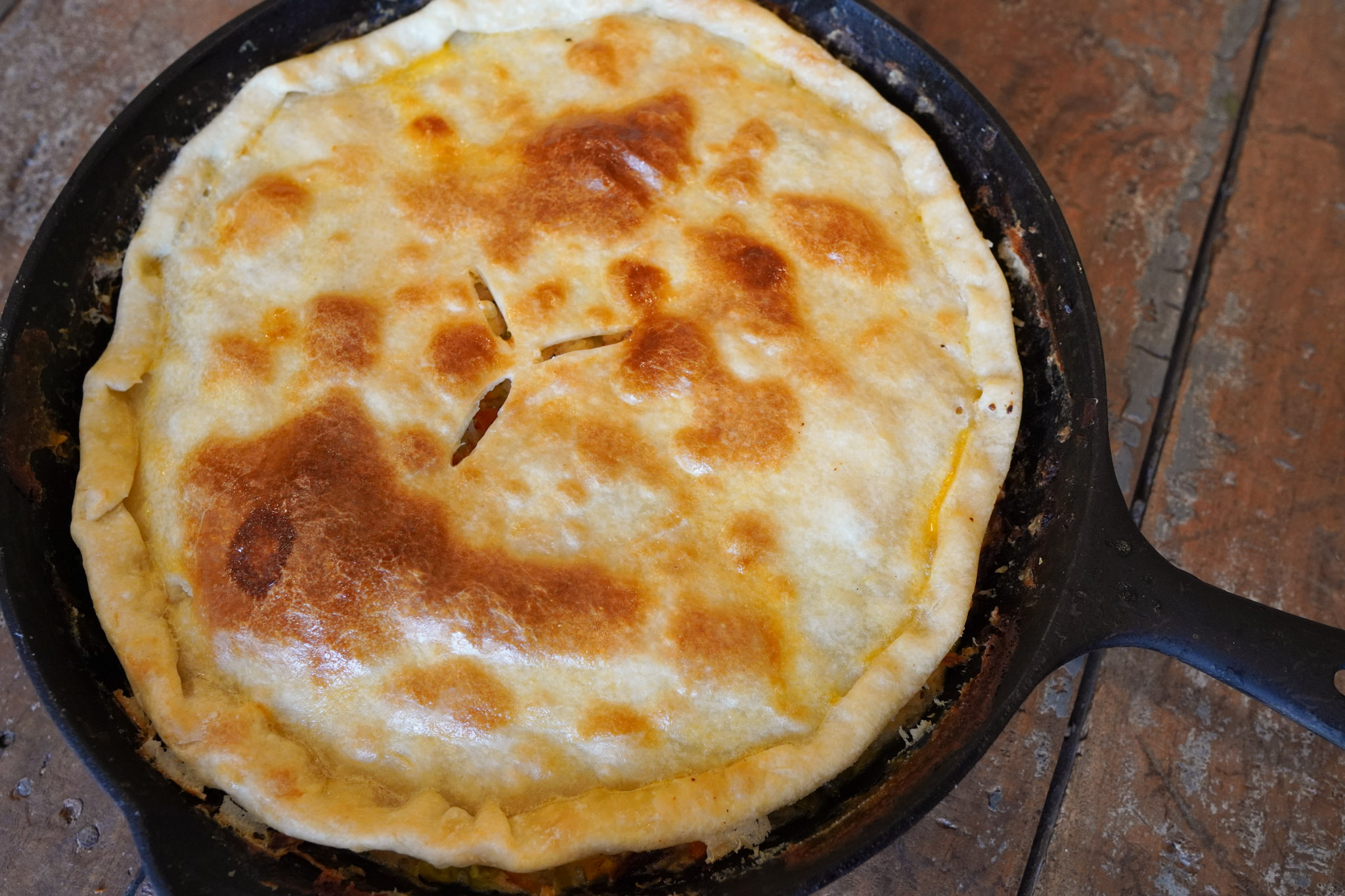 Golden crusted chicken pot pie baked to perfection in a large cast iron skillet sits on a tea towel on a wooden table top