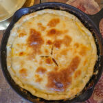 Golden crusted chicken pot pie baked to perfection in a large cast iron skillet sits on a tea towel on a wooden table top