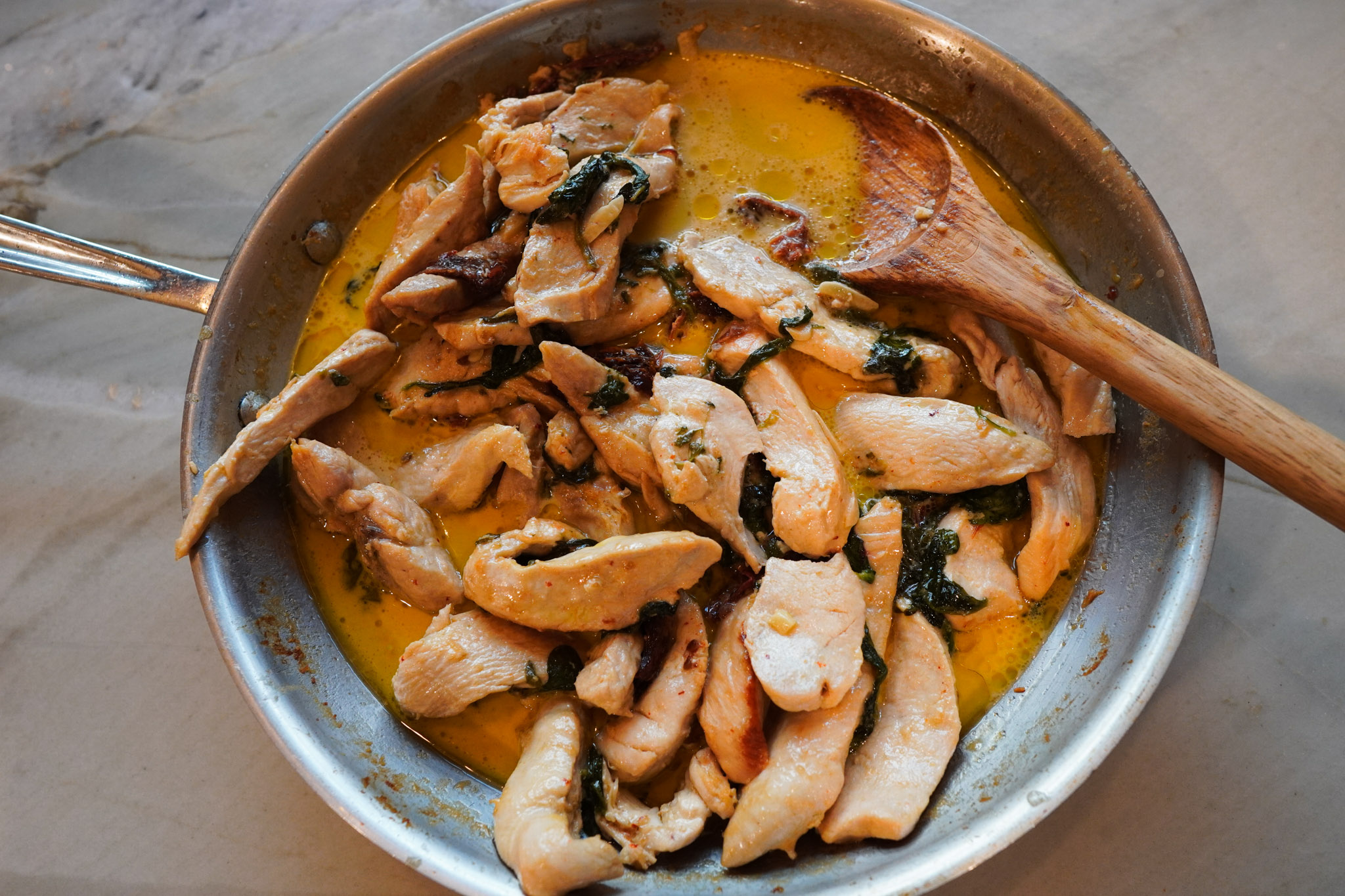 A skillet of creamy tuscan chicken with wooden spoon ready to serve