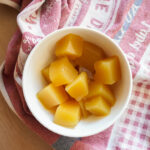 a white bowl of pineapple gummies sitting on a tea towel on a wooden counter top