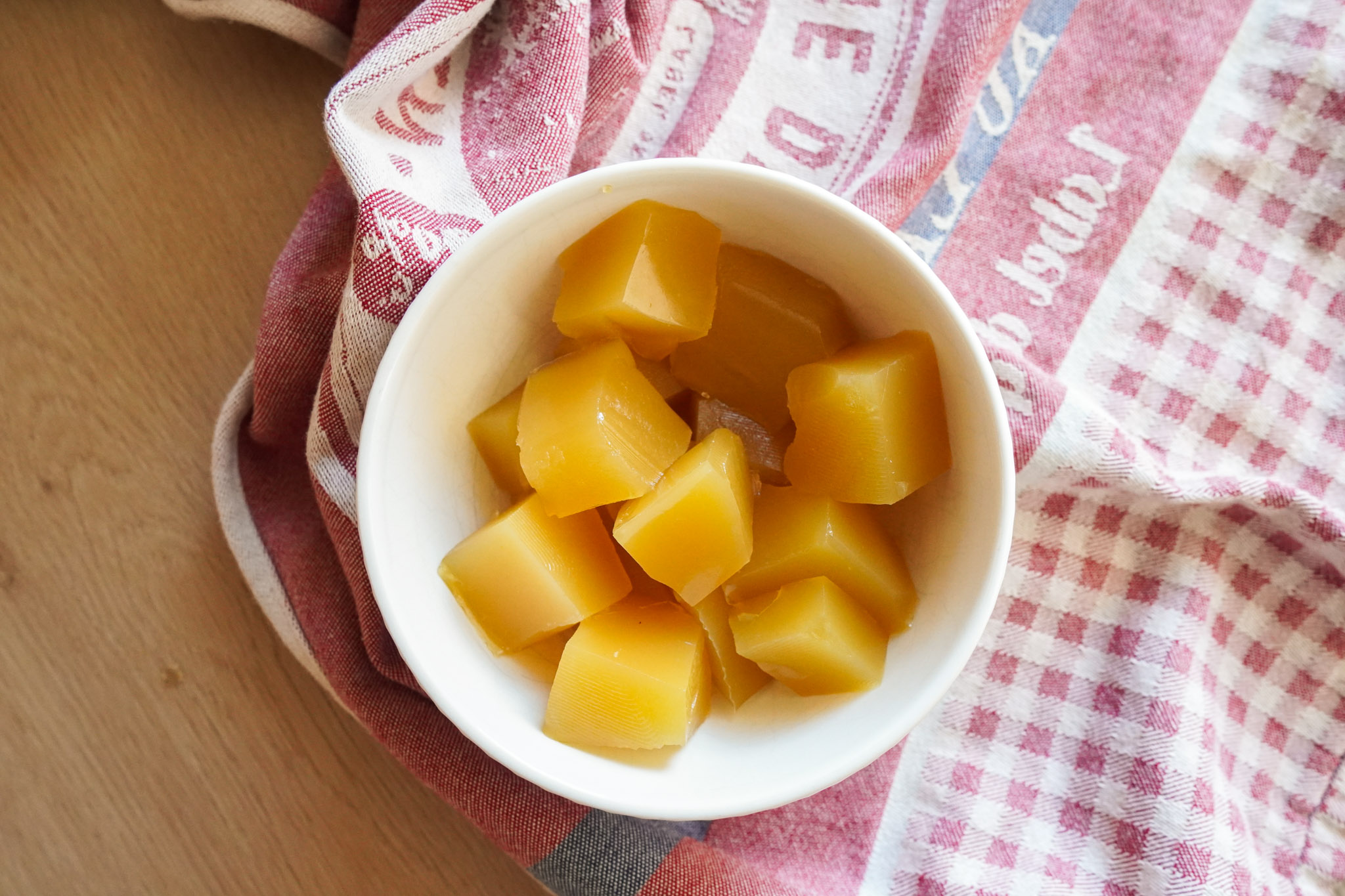 a white bowl of pineapple gummies sitting on a tea towel on a wooden counter top