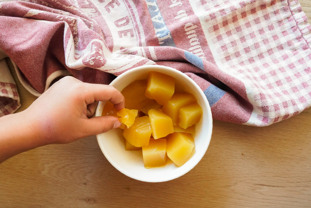 a hand reaches for a pineapple gummy from a white bowl sitting on a wooden counter top
