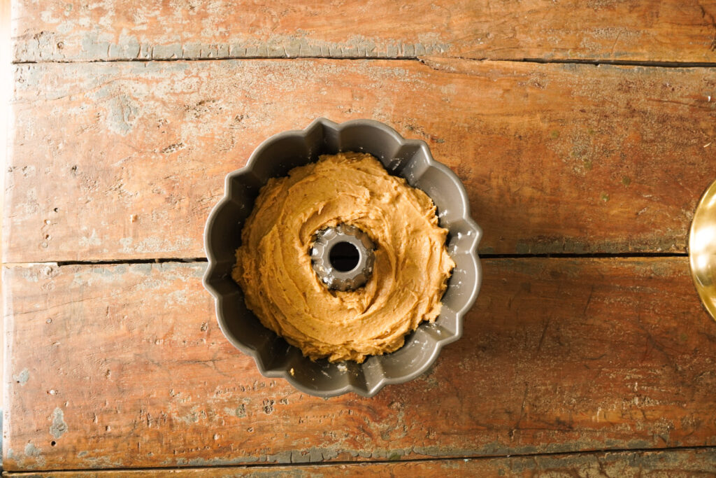 A bundt pan filled with apple spice cake batter sitting on a wooden table top ready to bake