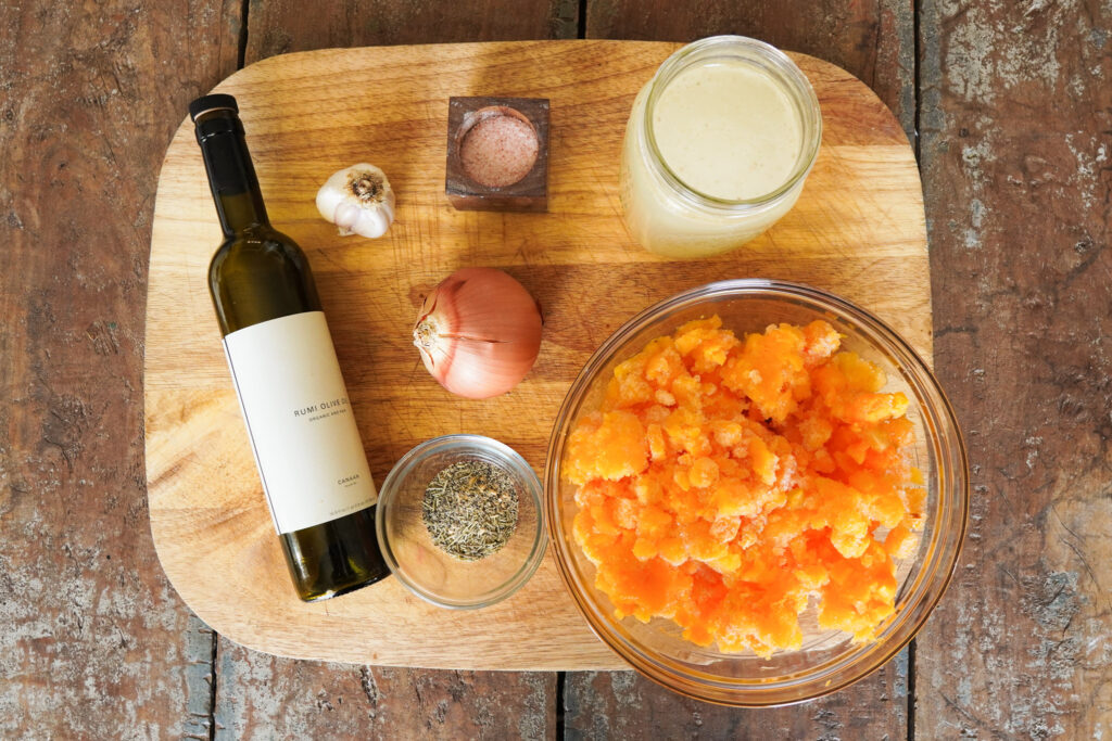 ingredients for butternut squash soup sitting on a wooden cutting board including squash, chicken broth, onion, garlic, and olive oil