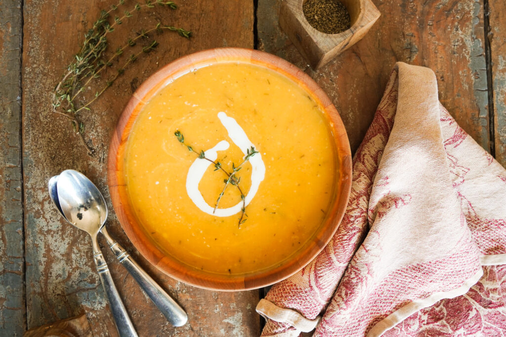 wooden bowl of cozy butternut squash soup sitting on a wooden table along with spoons and a tea towel