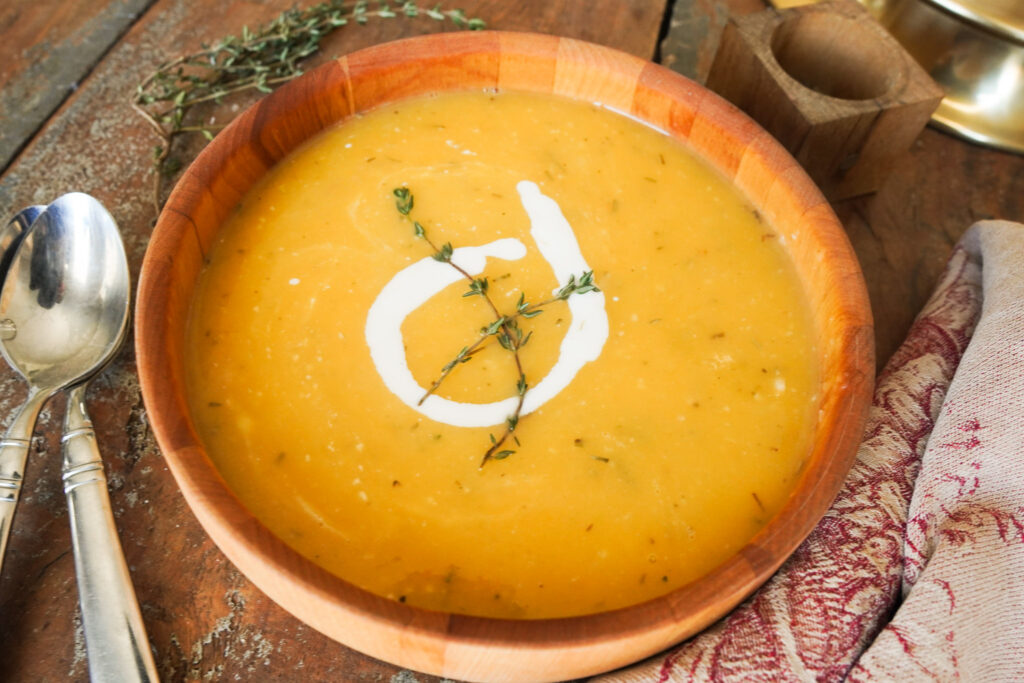 wooden bowl of cozy butternut squash soup sitting on a wooden table along with spoons and a tea towel