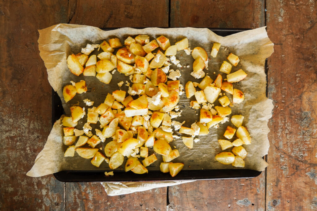Parchment lined cookie sheet filled with crispy potato chunks and feta cheese sitting on a wooden table top