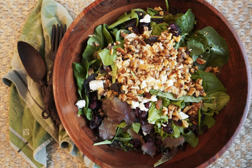 a large wooden bowl of winter salad sits next to wooden serving utensils