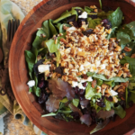 a large wooden bowl of winter salad sits next to wooden serving utensils