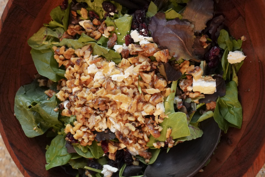 a large wooden bowl of winter salad with wooden serving utensils waiting to be mixed up